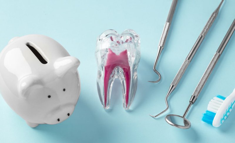 Tooth model with dental tools and piggy bank representing implant cost savings
