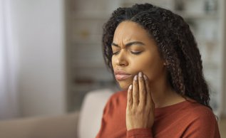 Young woman holding her jaw in pain due to an intermittent toothache at home